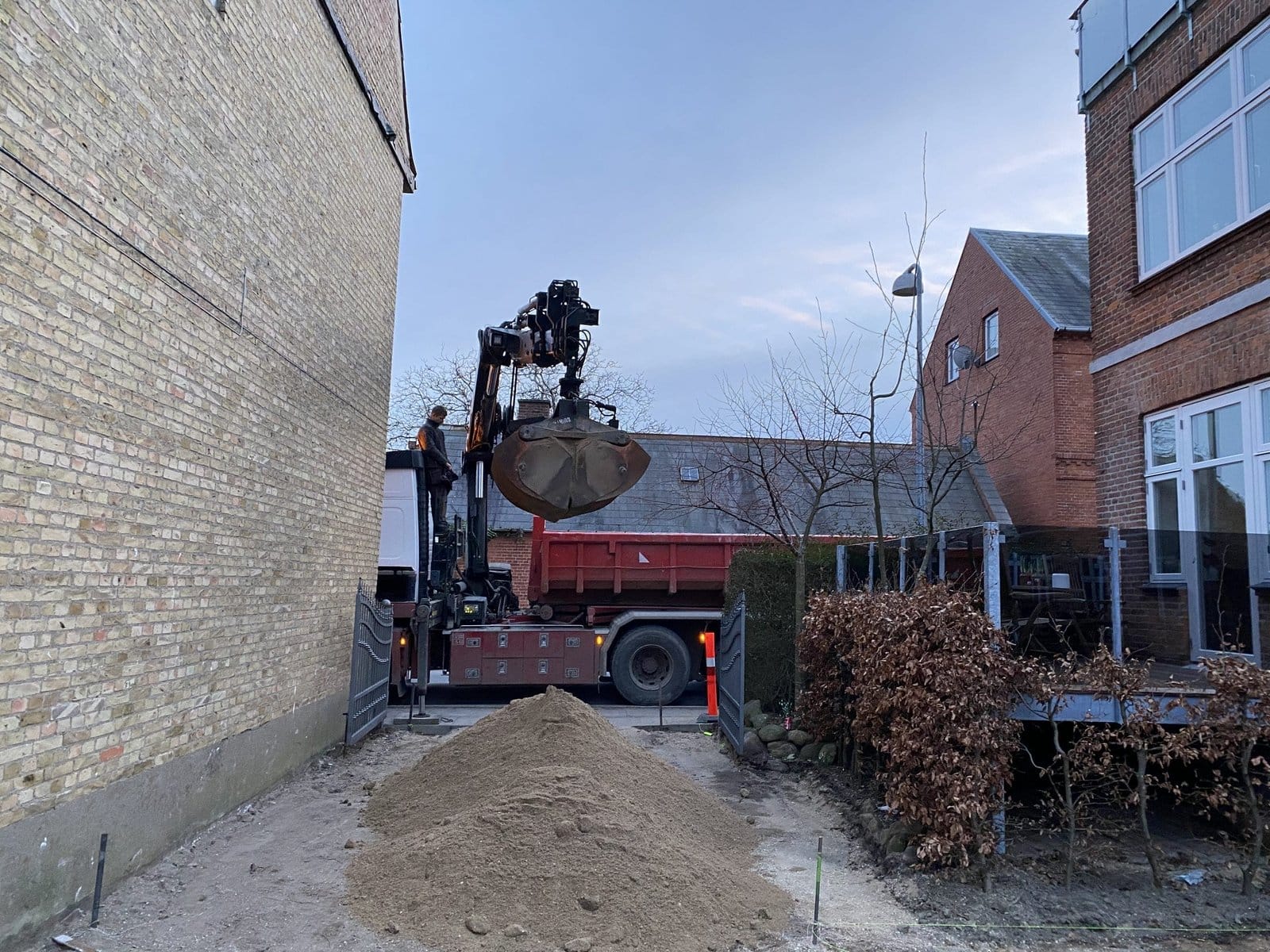 Lastbil med grab læsser sand mellem bygninger