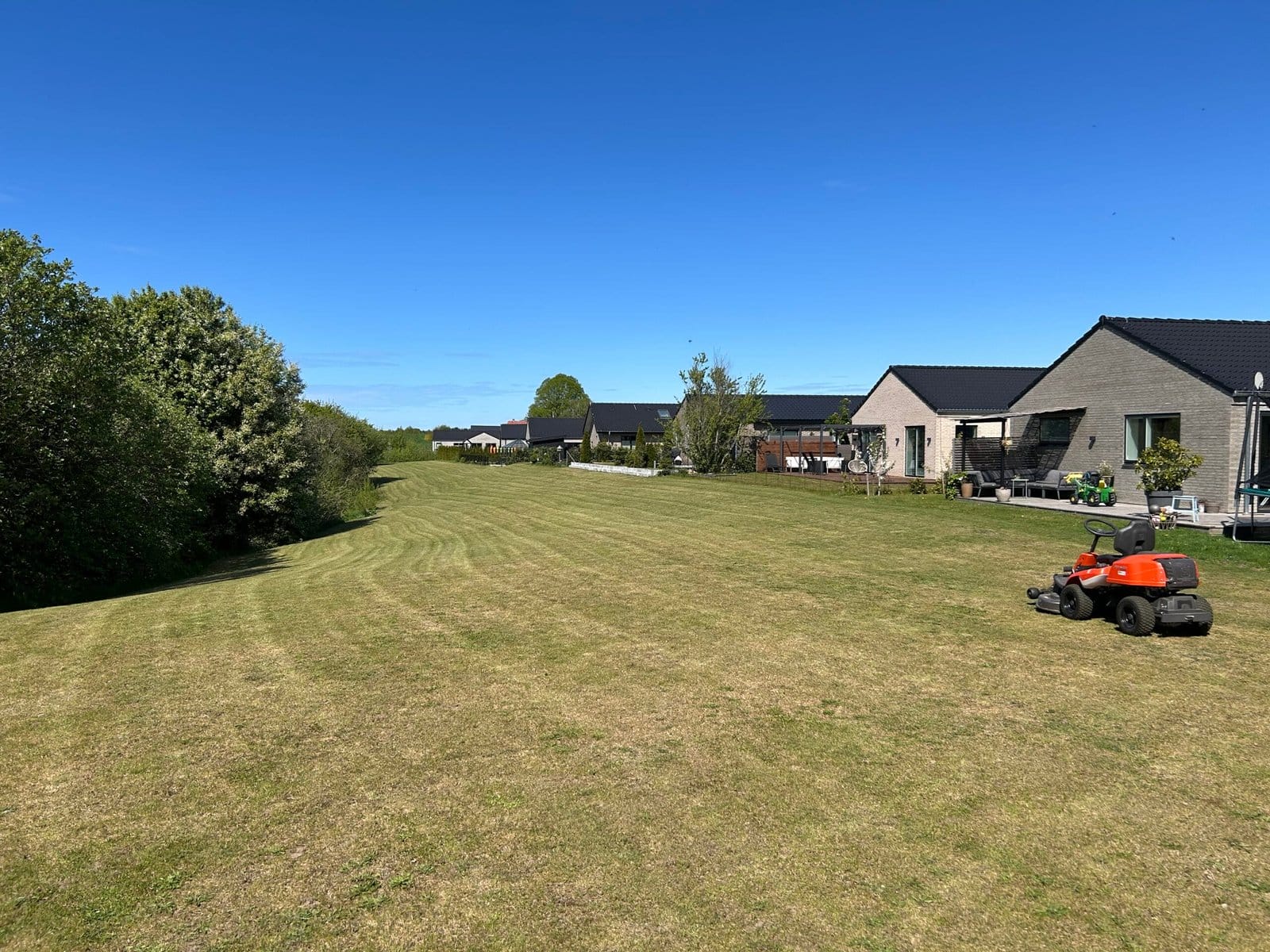 Græsslåmaskine på stor grøn plæne ved huse