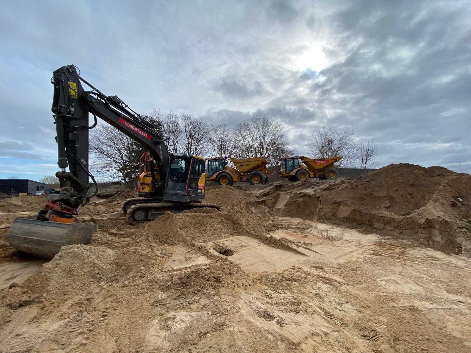 Gravemaskine og lastbiler arbejder på byggeplads